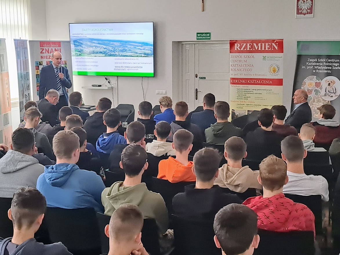 Uczestnicy spotkania siedzą w sali, Profesor Dudek omawia prezentację