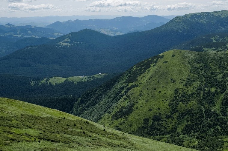 Panoramiczny widok na rozległe, wysokie góry widziane z wysokiego punktu obserwacyjnego – widoczne liczne górskie szczyty, doliny i surowy, naturalny krajobraz pod rozświetlonym niebem