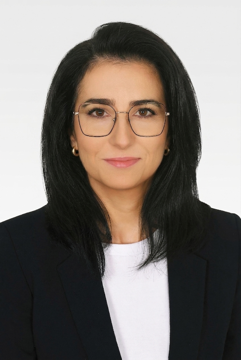 Portret kobiety o ciemnych włosach, ubranej w ciemną marynarkę i okulary.