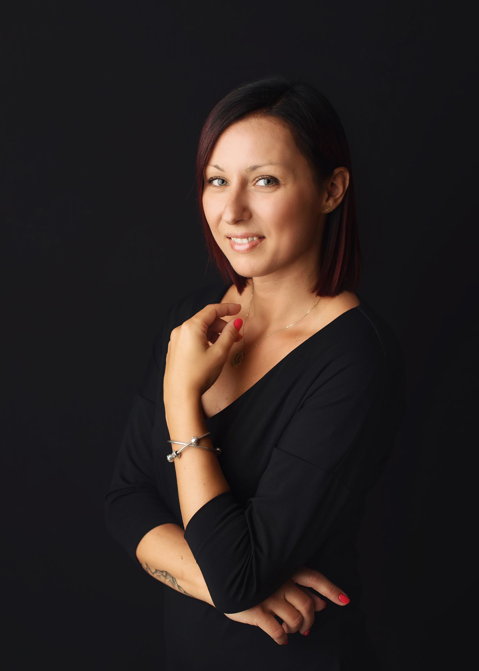 Portret uśmiechniętej kobiety z ciemnymi włosami na czarnym tle.