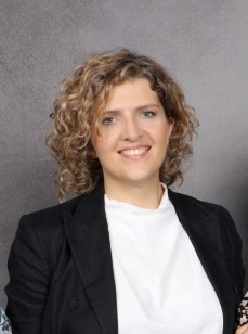 Kobieta o kręconych włosach, ubrana w białą koszulkę i czarną marynarkę