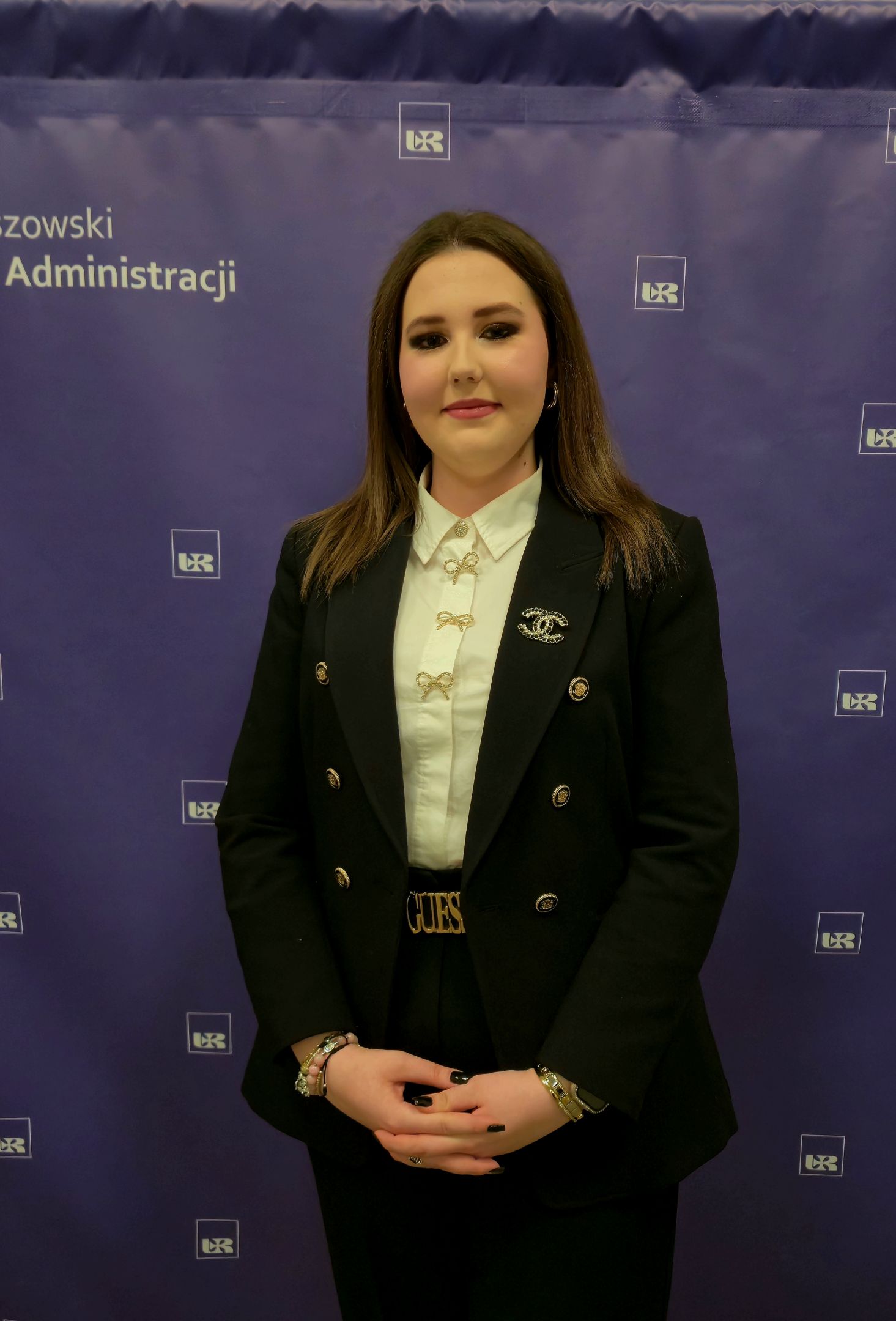 Kobieta o ciemnych włosach ubrana w marynarkę i koszulę, na tle z logo Uniwersytetu Rzeszowskiego i Wydziału Prawa i Administracji